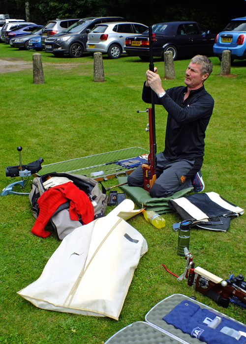 Photograph shows a competitor carefully preparing his Feinwerkbau rifle, amidst all his kit, prior to competition.