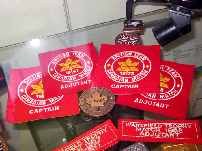 Photograph shows various cloth badges and medals relating to the British Team's participation in the Canadian Match series of competitions.